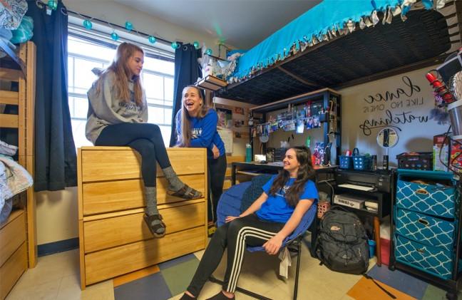 Three students talking and laughing in their dorm room
